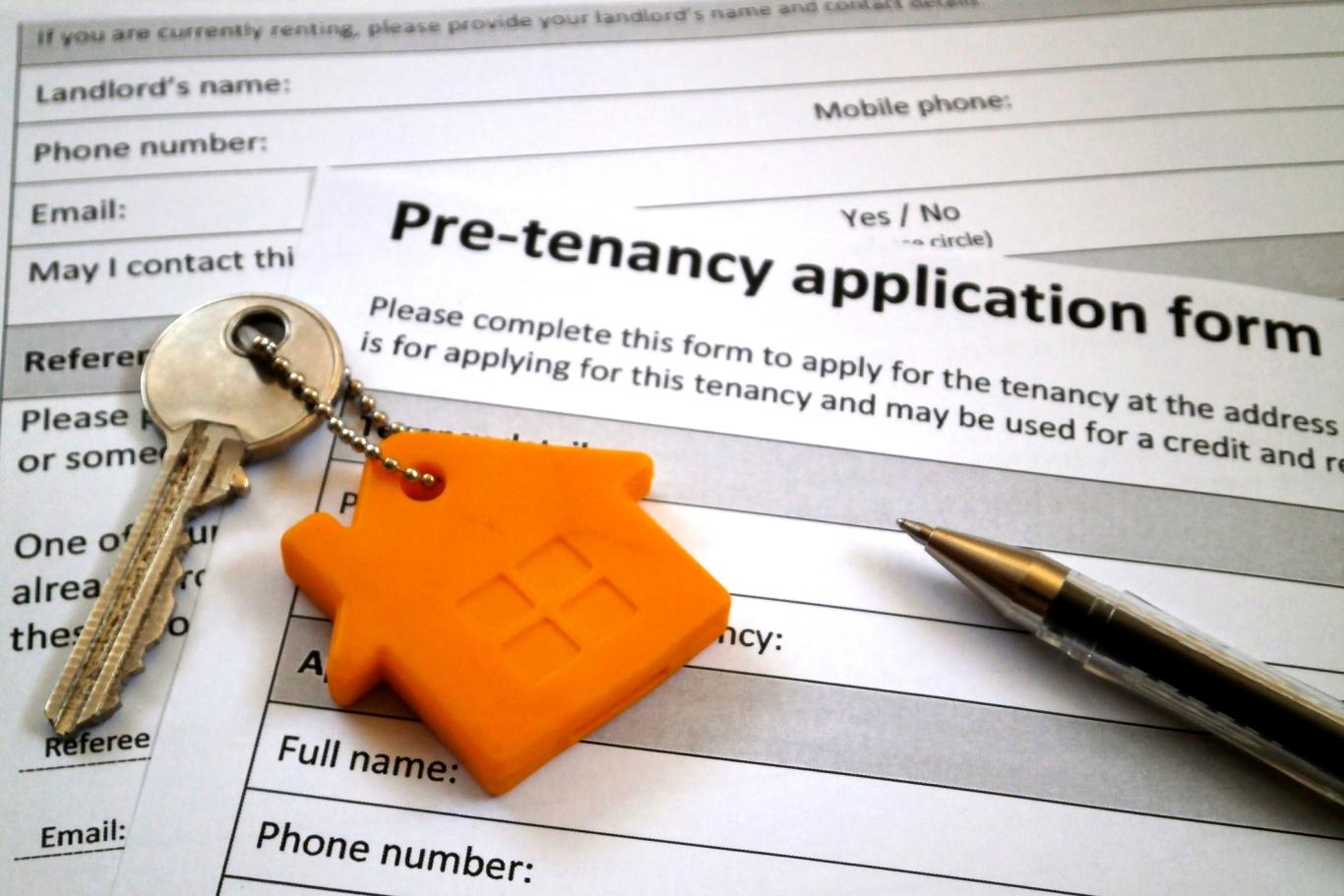 A key with an orange house keychain and a pen rest atop an apartment application form.