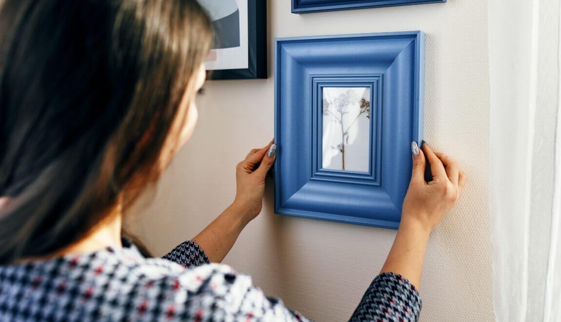 A woman positions a small photo in a blue frame on the wall.
