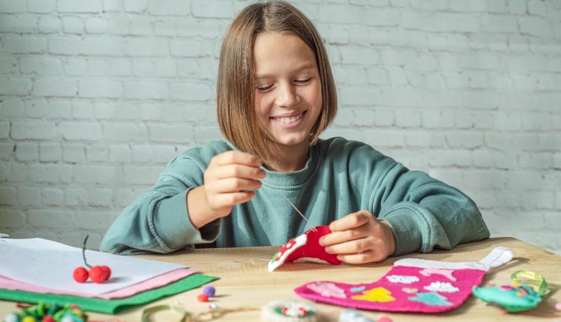 A child pulls thread through a handmade Christmas stocking.