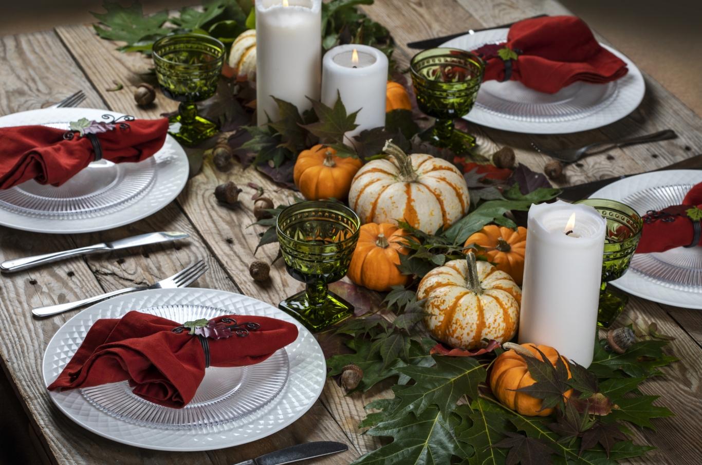 A dinner table set for Thanksgiving with candles and pumpkins.