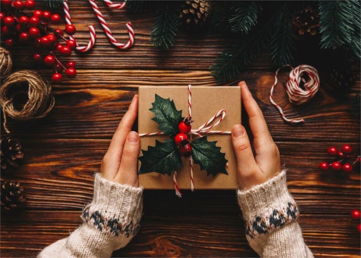 Close-up of hands holding a plainly wrapped gift with decorative handmade bow.