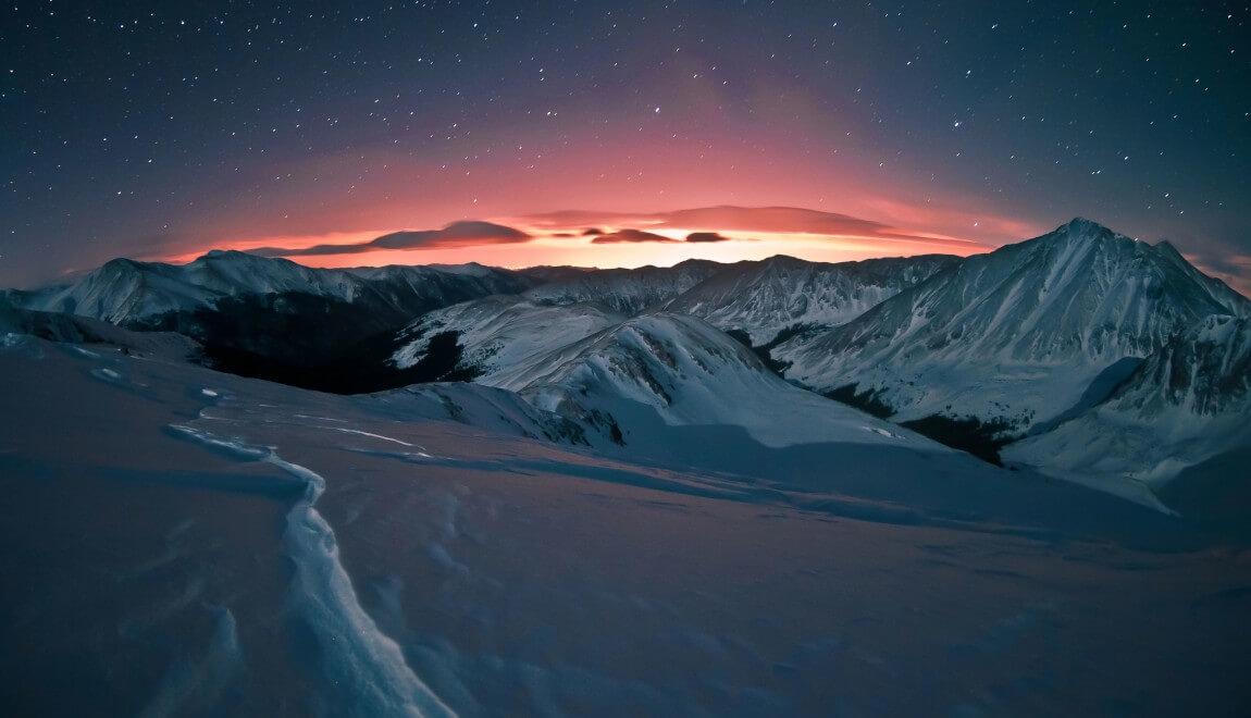 Snow-capped mountains of Colorado against a pink sky.