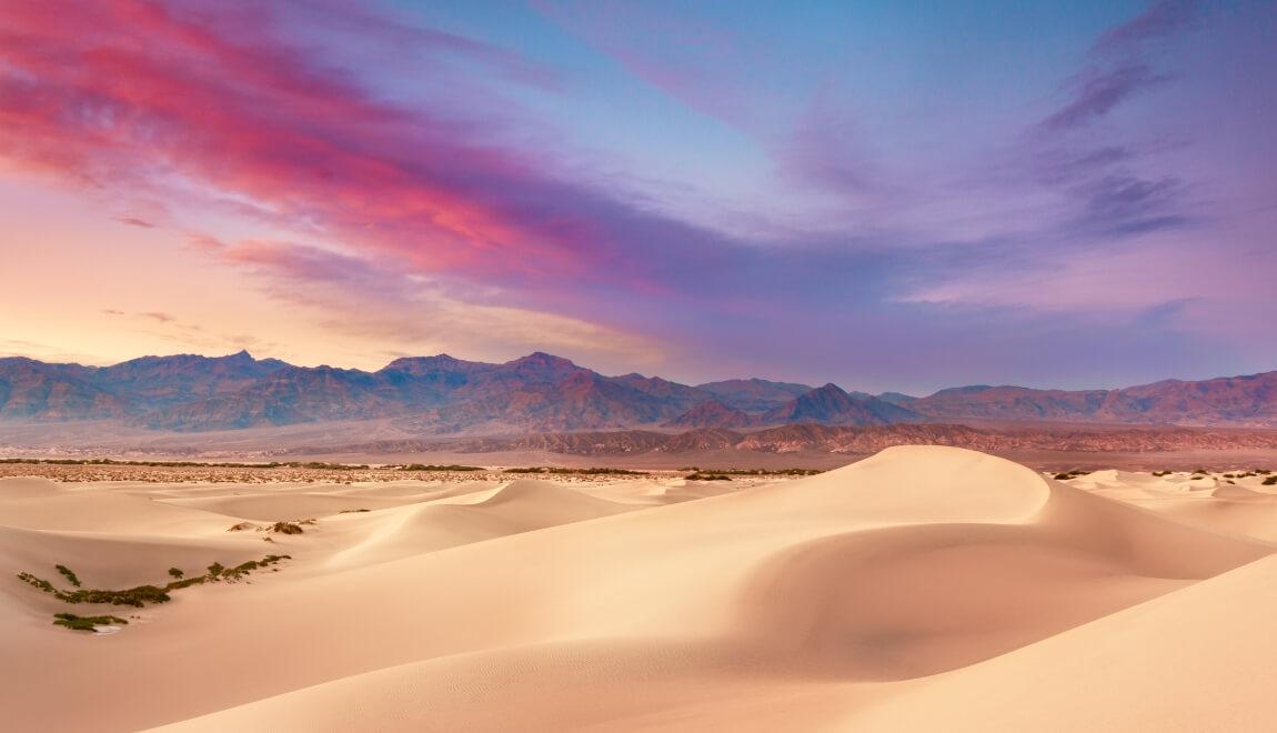 Sand dunes and mountains against a pink sky in Death Valley National Park.