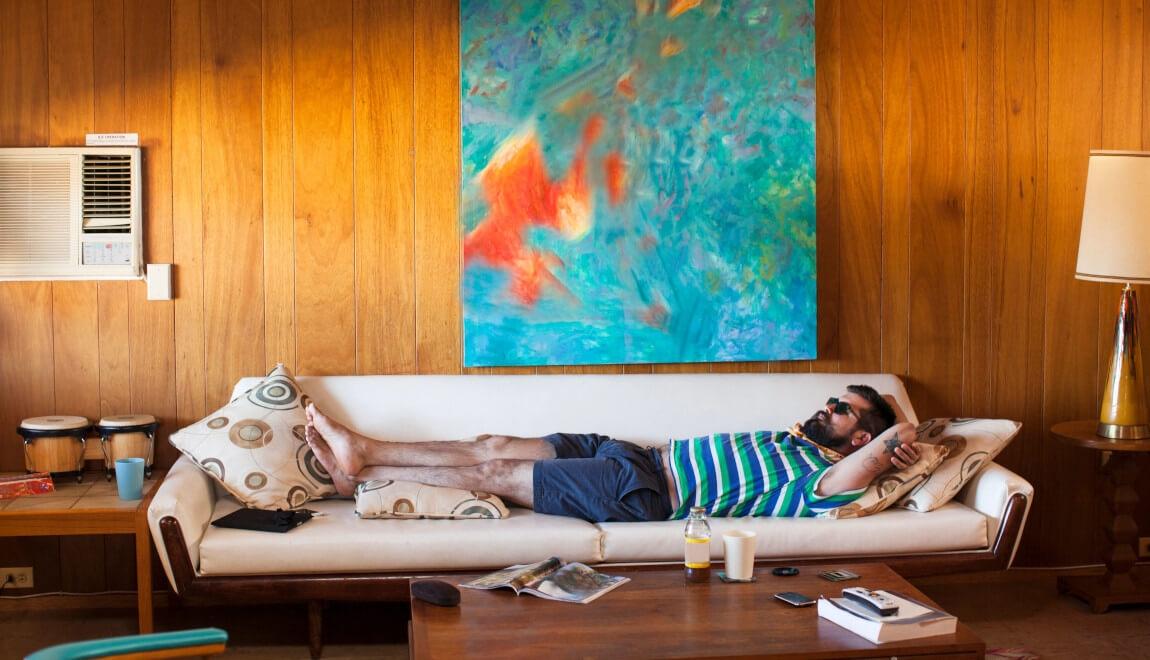 A man lounges on a couch wearing shorts and sunglasses.