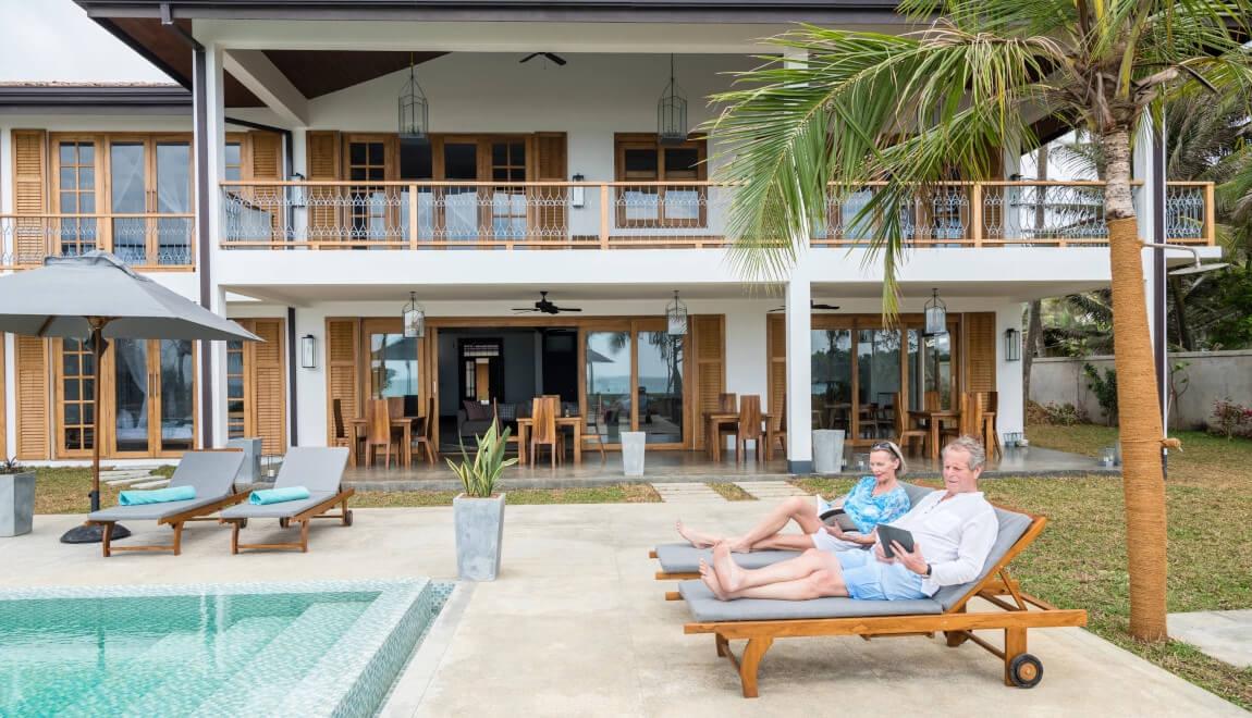 An older couple relaxes next to an outdoor swimming pool.