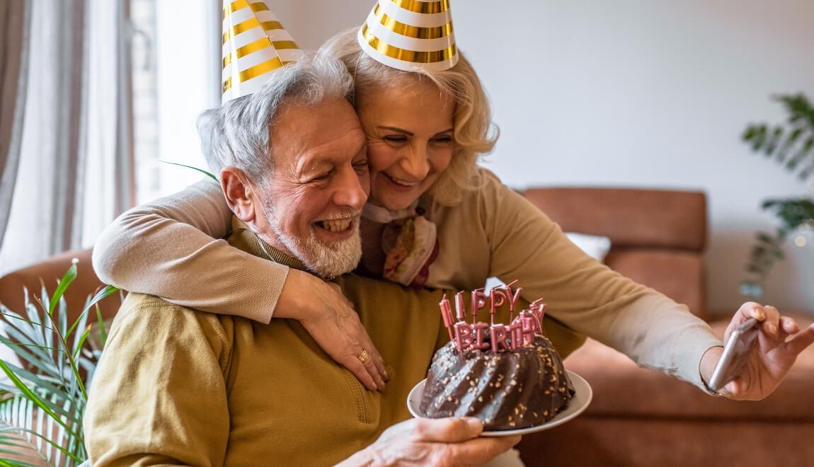 An older couple wearing party hats looking at a birthday cake.