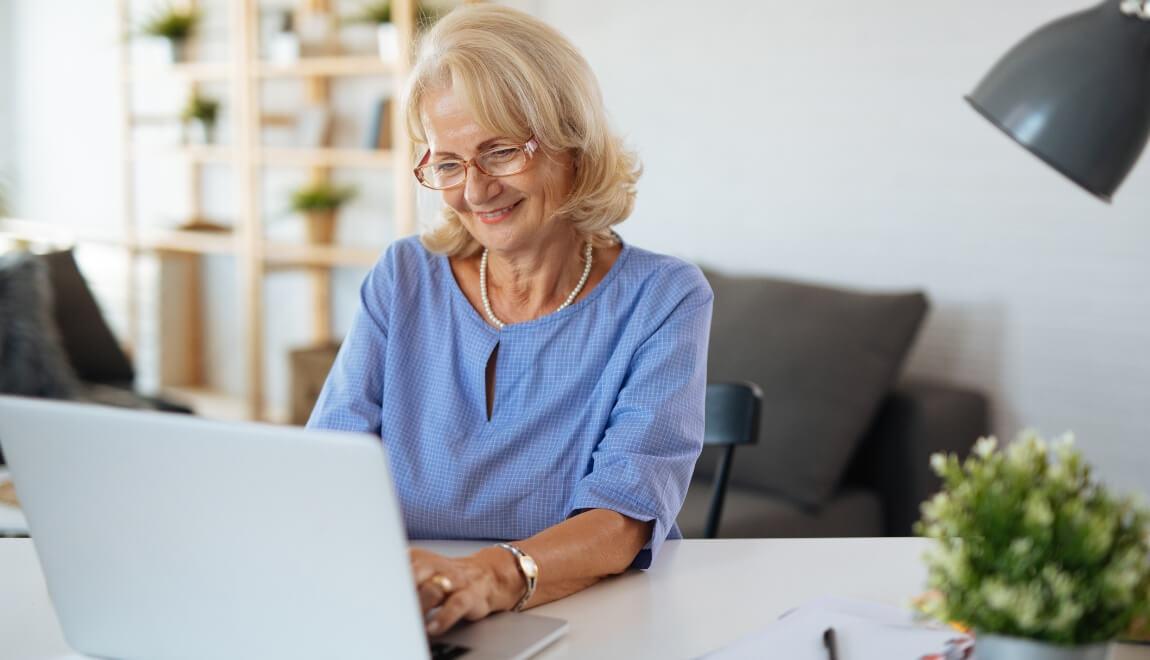 An older woman sits at a desk with a laptop computer.