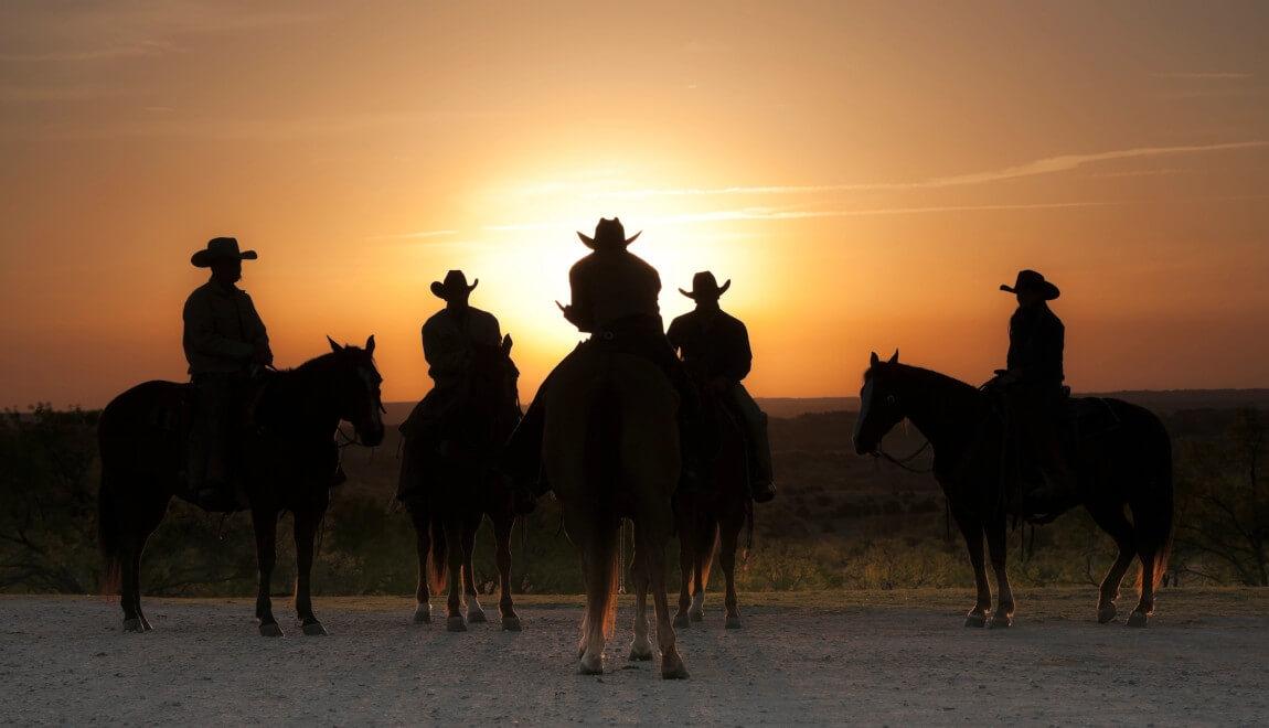 Cowboys in shadow against a setting sun.