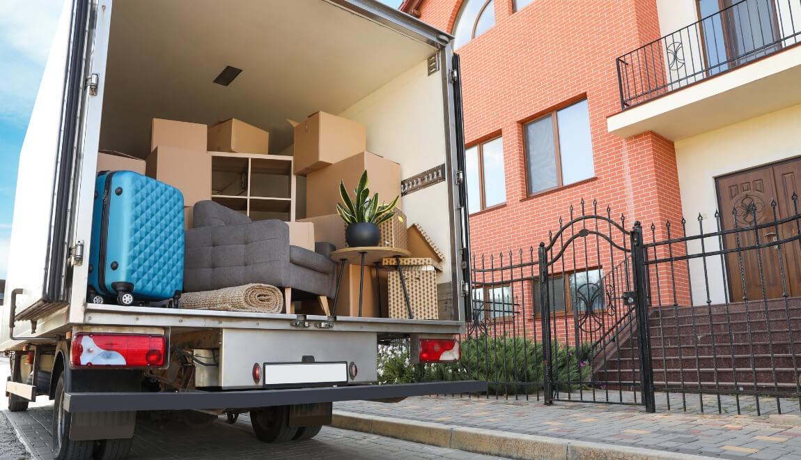 An open moving truck in front of an apartment building, loaded with boxes and furniture.