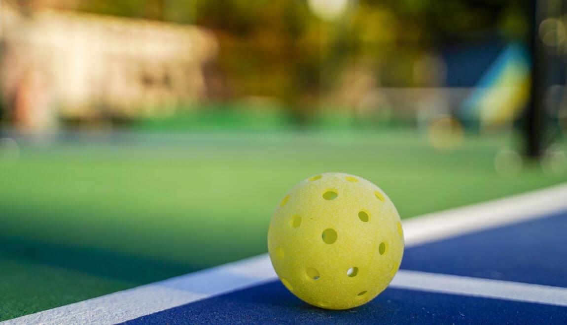 A pickleball sitting on the court with a blurred background. 