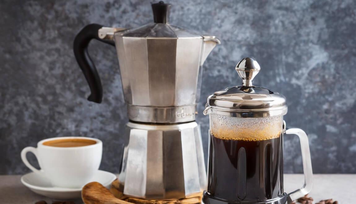 A moka pot, French press, and cup of espresso sit on a table