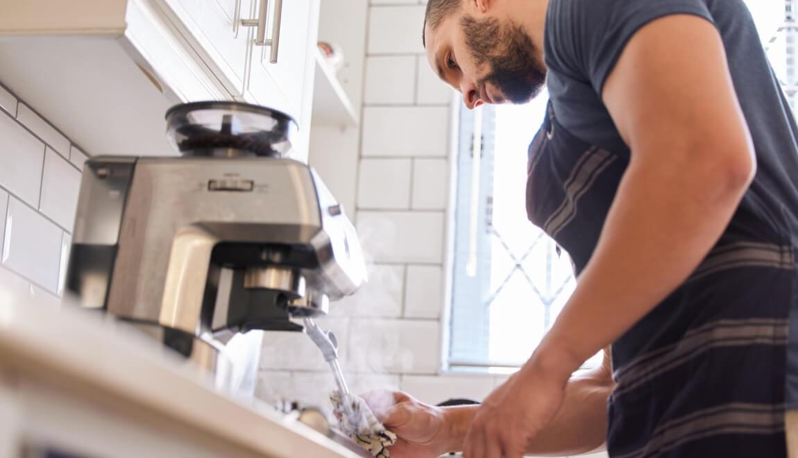 Man cleaning the steaming wand on the espresso machine in his kitchen