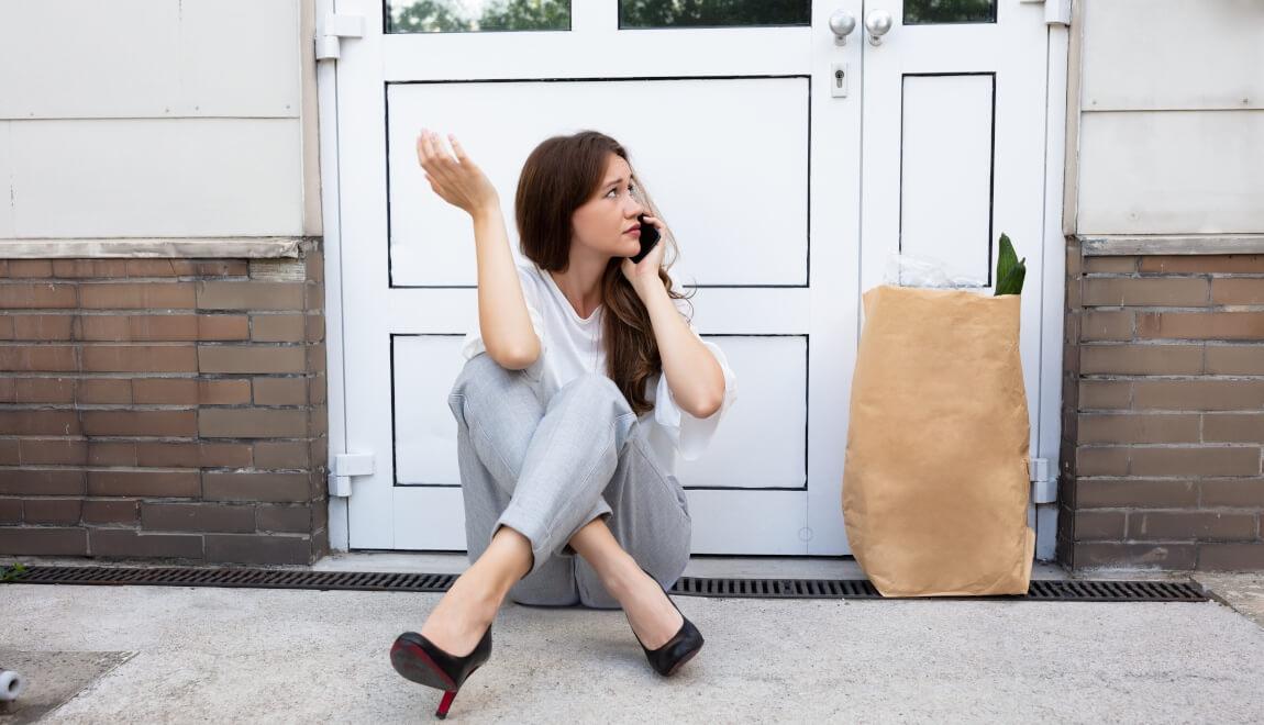 A frustrated woman sits outside of her locked apartment.