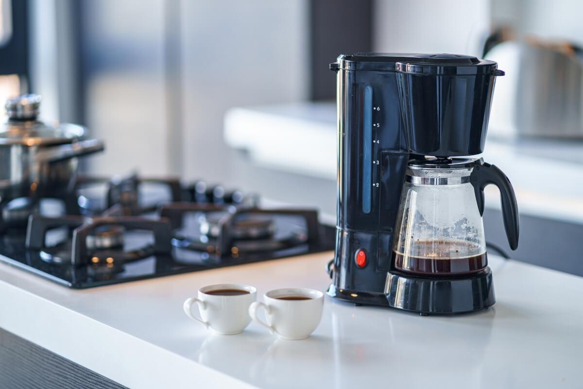 A coffee maker and two mugs filled with coffee sit on a kitchen counter.