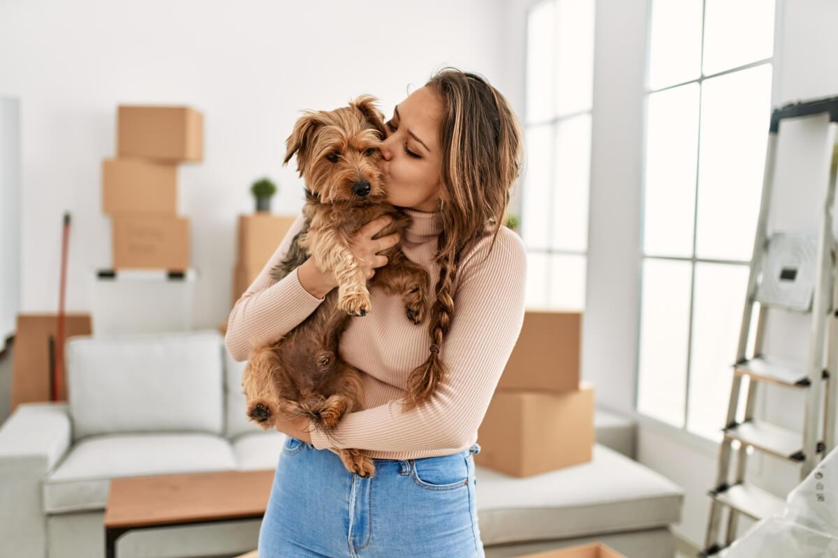 A young woman hugs a small dog in a new apartment.