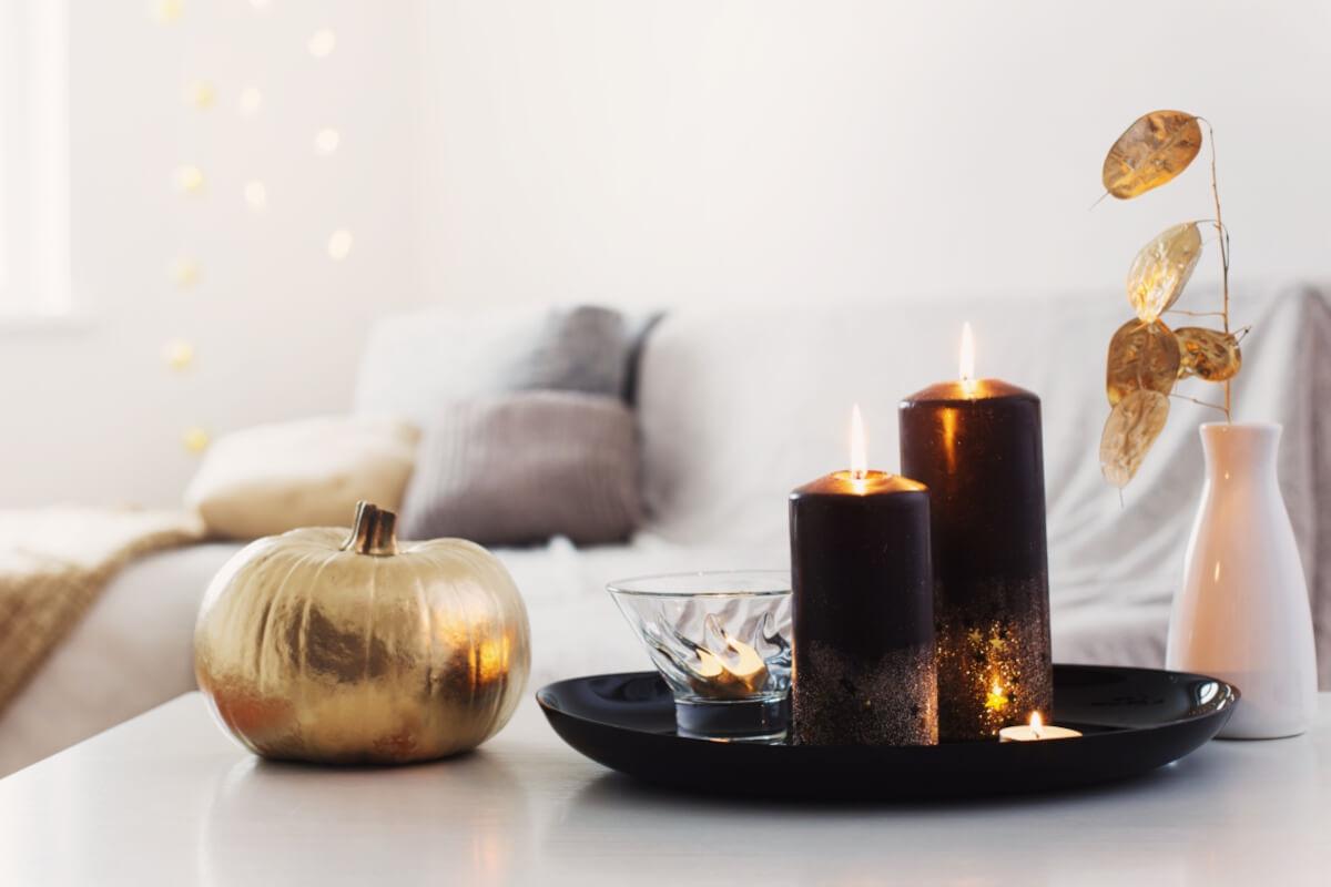 A decorative vase, gold-painted pumpkin, and candles sit on a coffee table with a couch in the background.