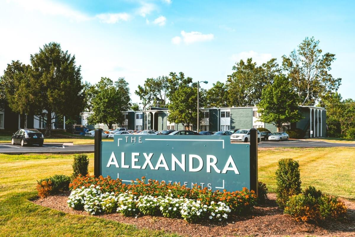 A sign for The Alexandra Apartments is surrounded by flowers.