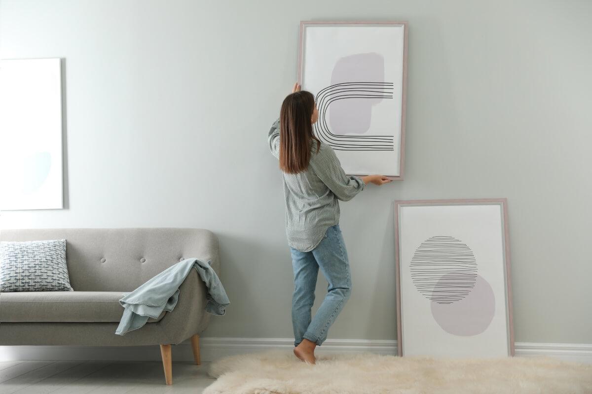 A young woman hangs abstract art on the walls of her apartment.