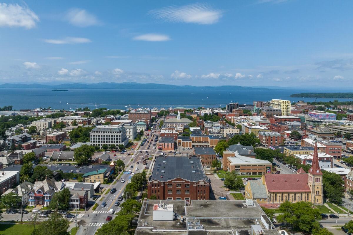 An aerial view of Downtown Burlington shows Lake Champlain and mountains in the distance.