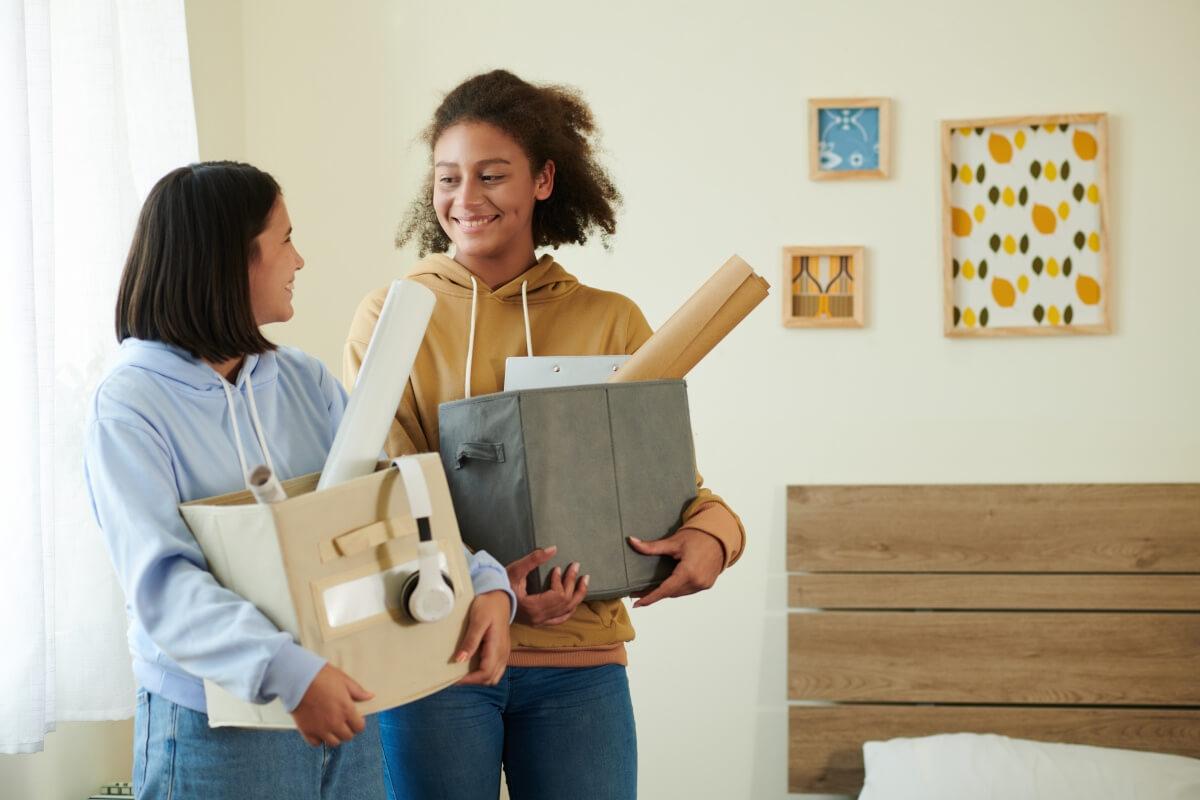 Two young women carry boxes into their new apartment.