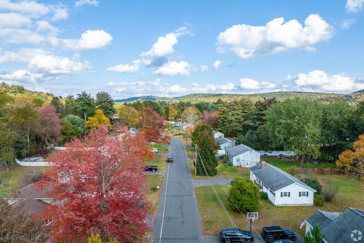 An aerial view of a residential neighborhood shows fall foliage and mountains in the distance.