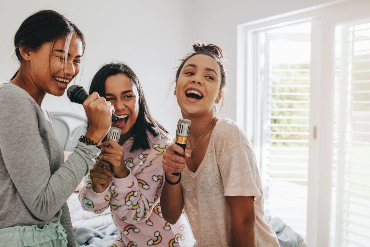 Three girls sing karaoke in a bedroom.