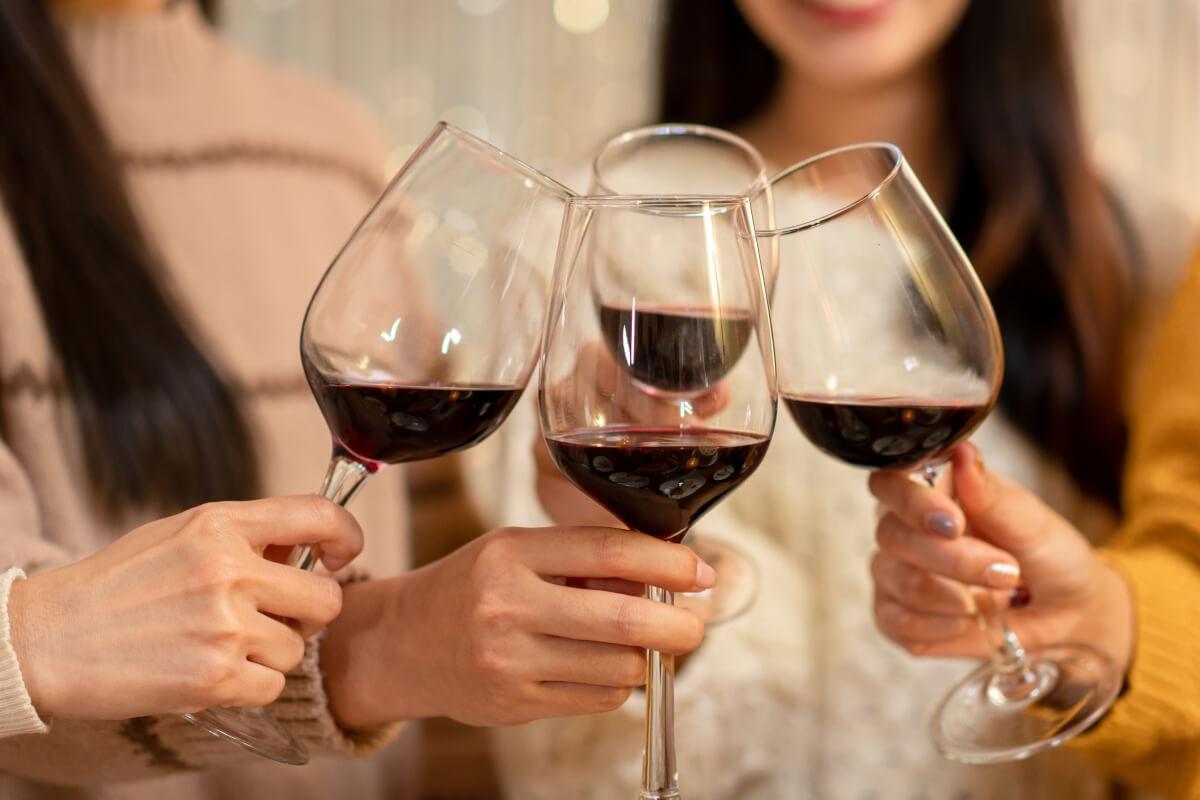 Four women clink glasses of red wine.