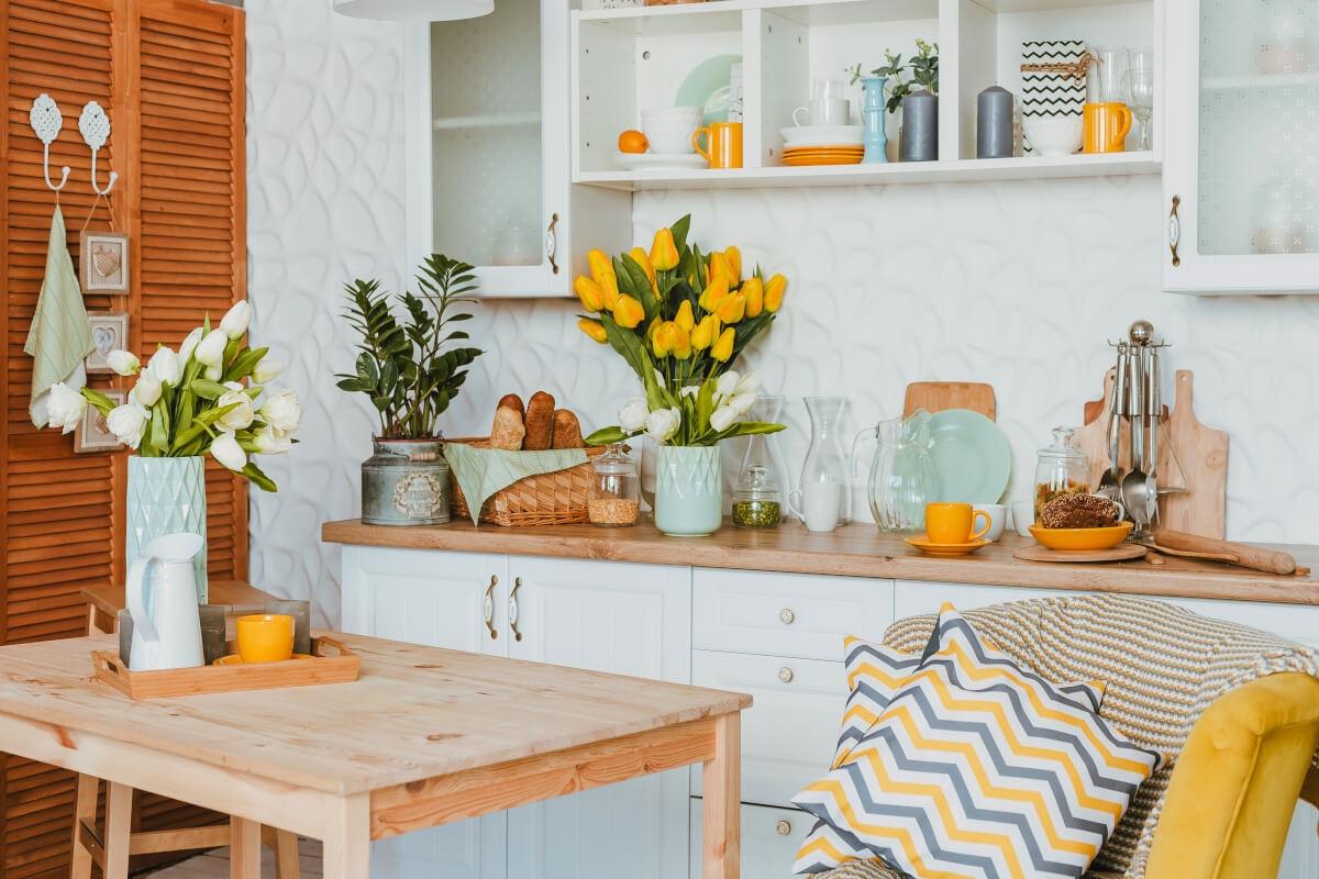 An apartment kitchen is decorated various flower bouquets and bright shades of yellow.
