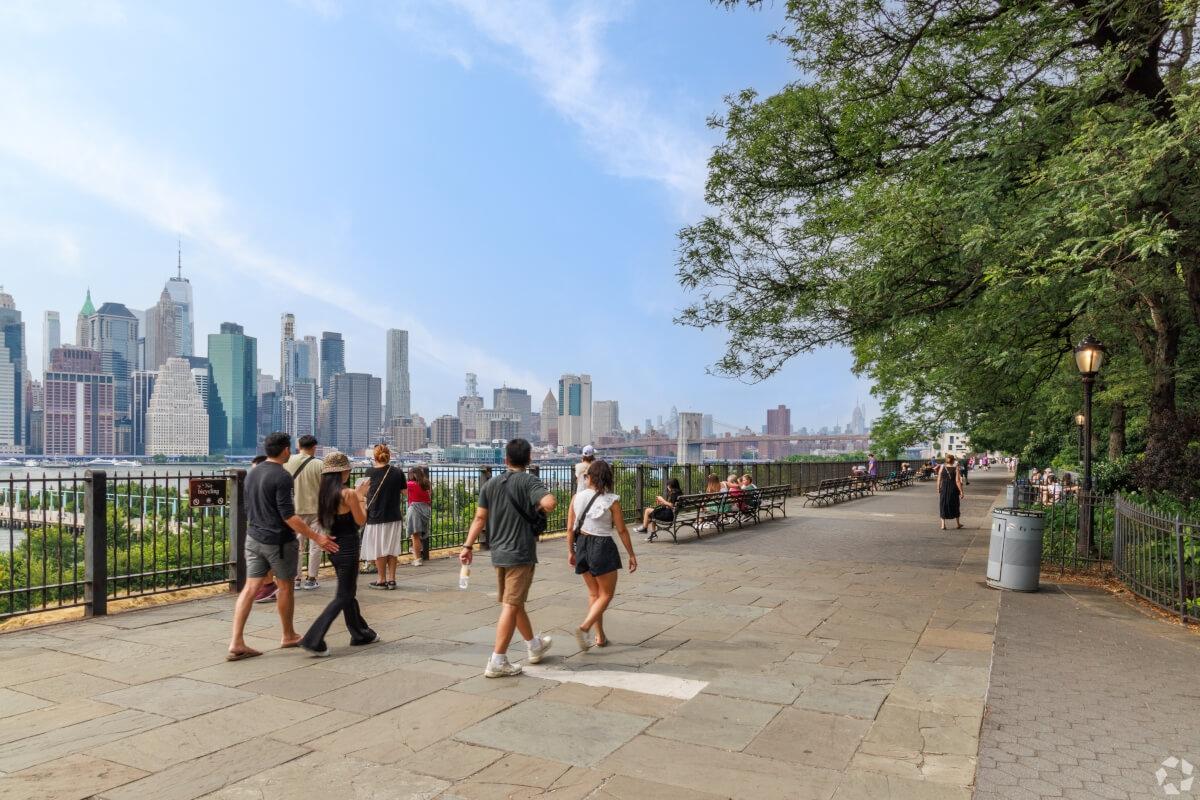 Visitors and residents walk along the Brooklyn Heights Promenade with the Brooklyn Bridge and Manhattan in the background.