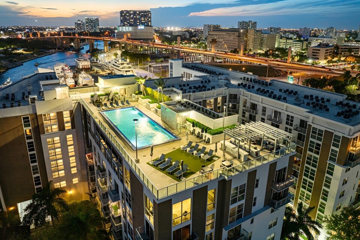 Lounge chairs on artificial grass and a grilling station are next to a rooftop pool.