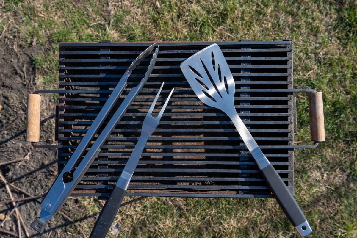A spatula, grill fork, and tongs sit on a small grill.