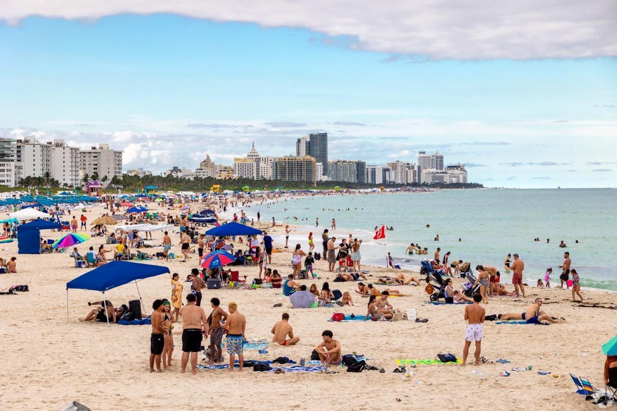 Crowded beach scene in Miami Beach with high-rise Art Deco buildings and a vibrant coastline — perfect for renters seeking walkable, cultural living near Collins Park