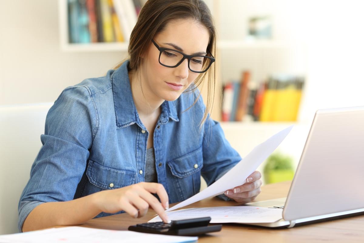 Woman budgeting using paper, calculator, and laptop.