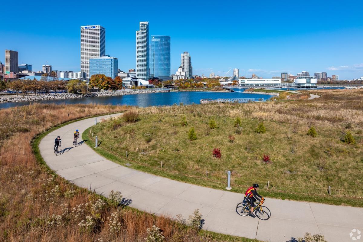 Cyclists ride along a scenic Lakeshore State Park trail with downtown Milwaukee skyline views, ideal for apartment dwellers seeking outdoor recreation.