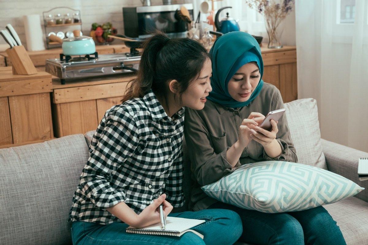 Two roommates sitting on a couch reviewing lease documents on a smartphone, representing flexible lease options for shared housing.