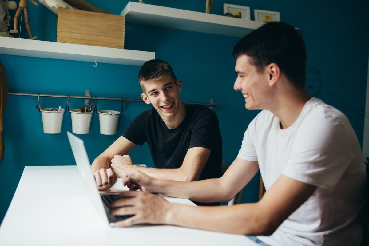 Two roommates discussing finances at a desk with a laptop, highlighting how to split rent based on bedroom size in a shared apartment.