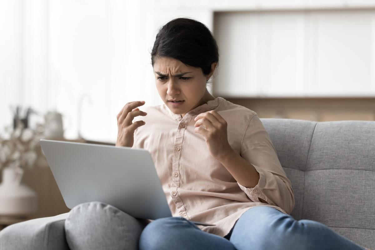 A frustrated young woman looks at something shocking on her laptop.