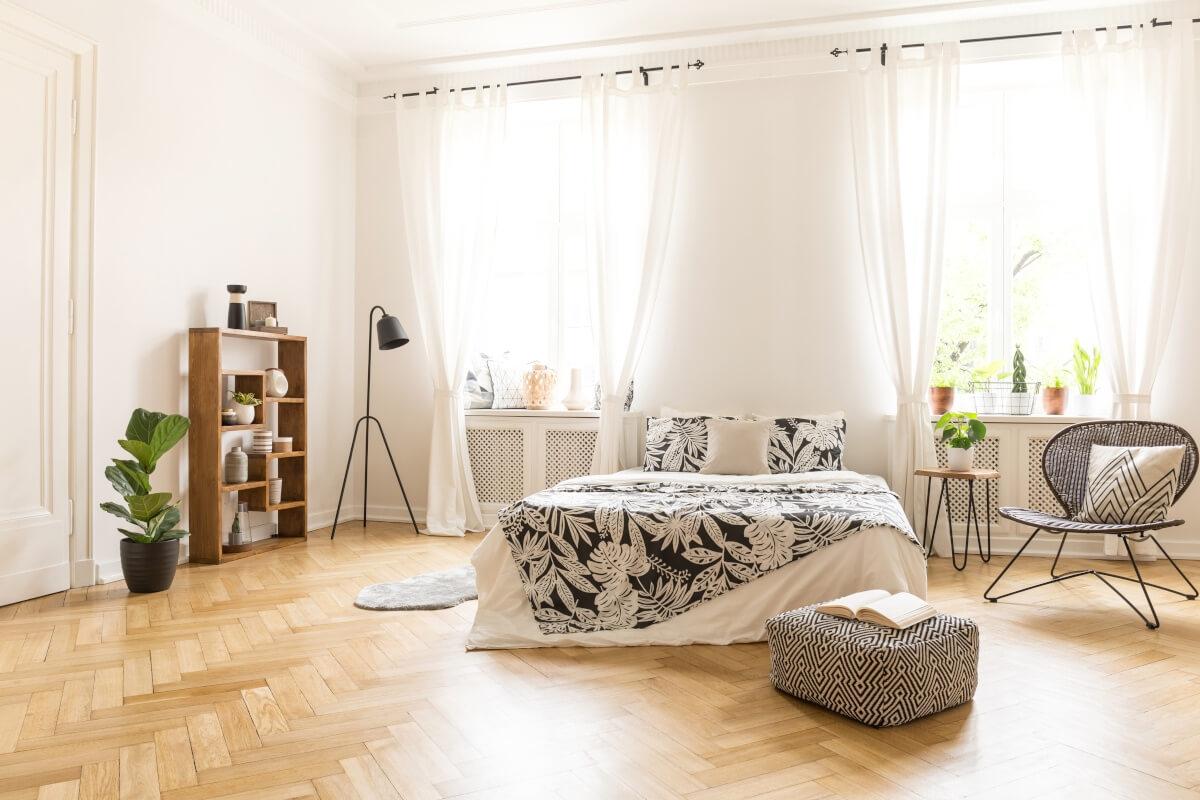 A view of a bedroom in a luxury apartment with high ceilings and large windows.