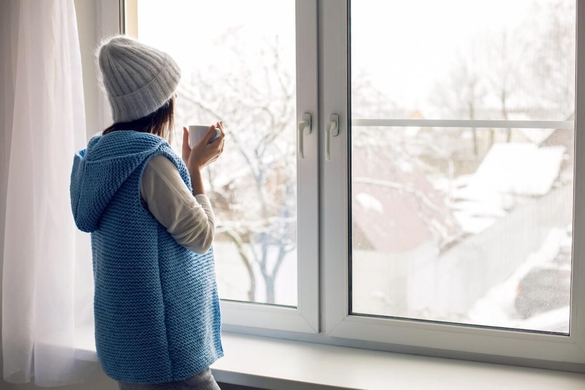 Woman sips her coffee and watches winter weather from her window.