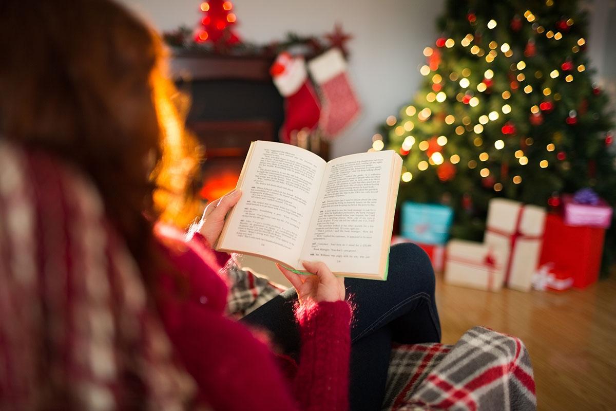 Woman reading book on couch in front of Christmas tree.