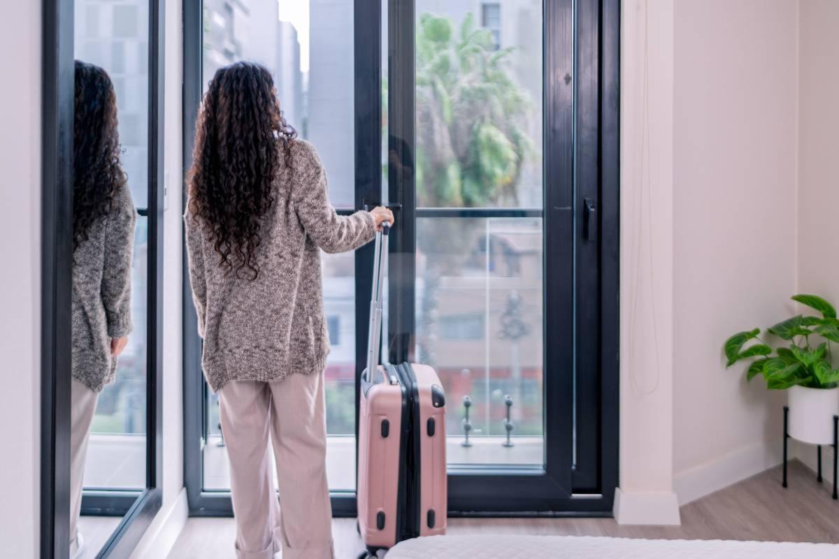Woman looks out the window with her suitcase by her side.