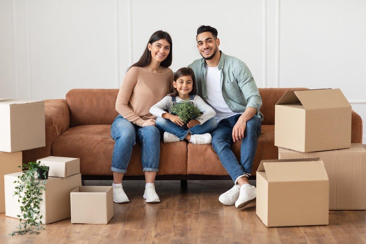 A family of three sitting on a sofa in the middle of moving boxes