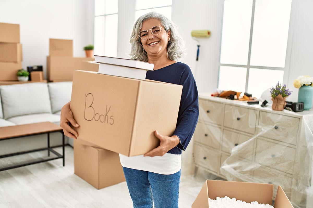 Older woman holding boxes as she is packing up her apartment.