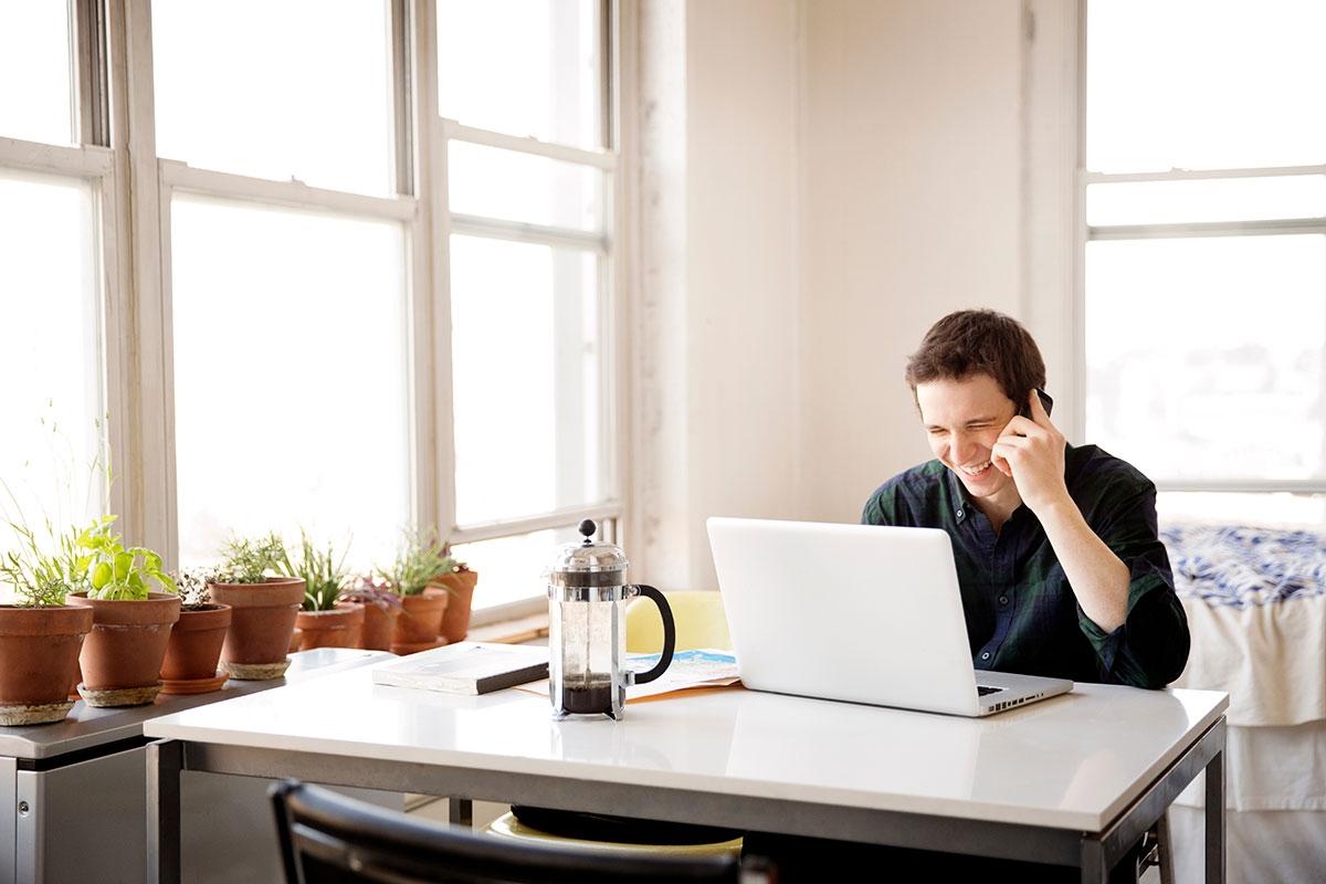Man talking on his phone with his laptop in front of him as he schedules moving tasks.