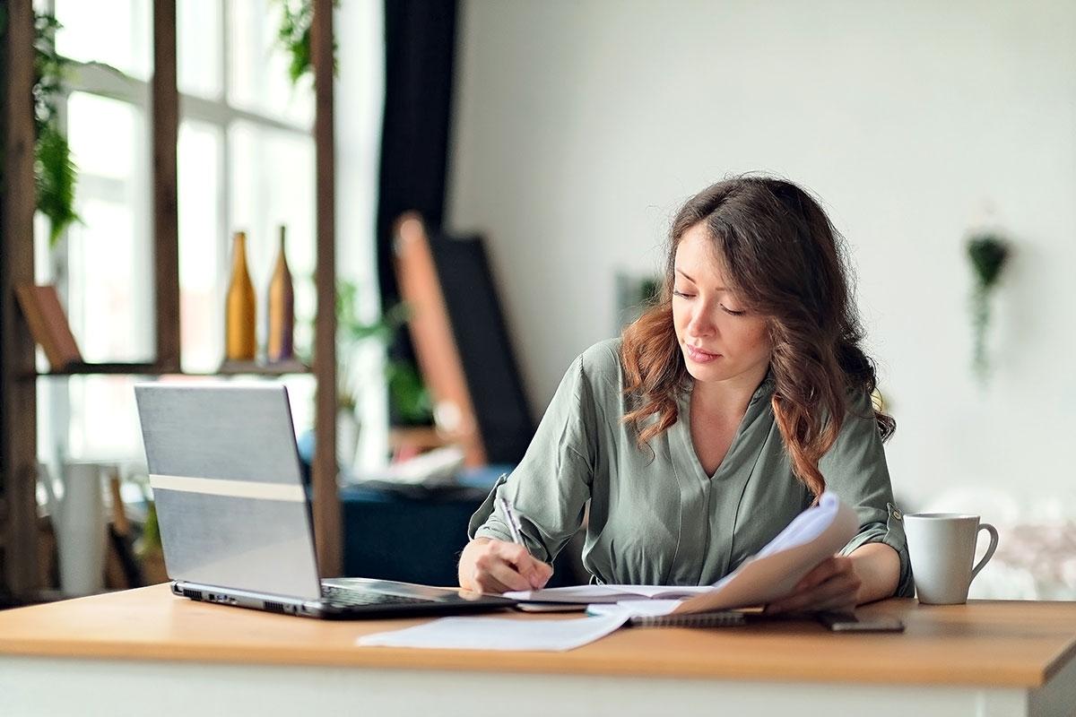 A lady taking notes on in front of laptop as she researches apartments.