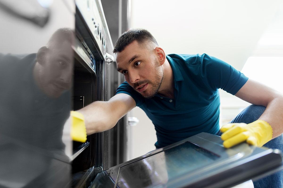 Man cleaning the inside of his stove with gloved hands.