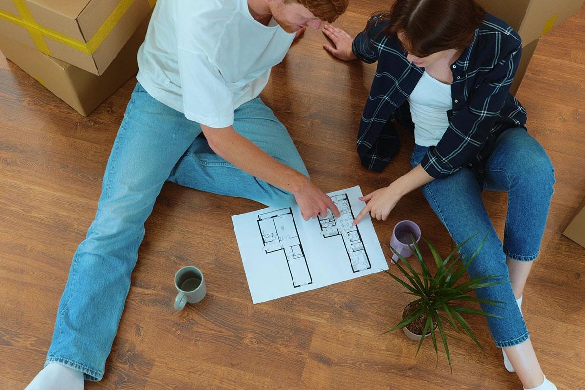 Couple sitting on floor and looking over floor plan together.
