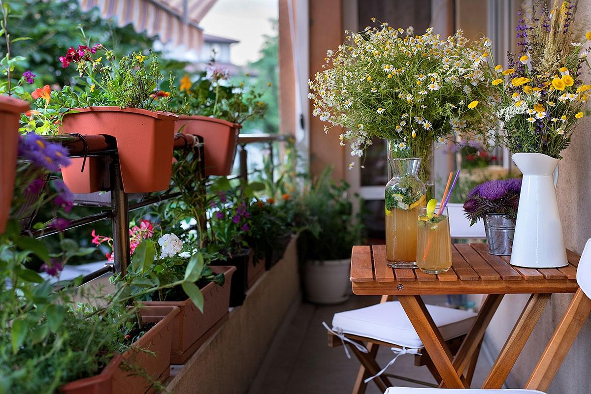 A balcony covered in plants with a little table and chairs that has vases and flowers on top.