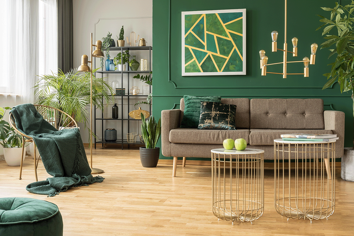 Living room with green walls contrasted against a light wood floor. There are geometric patterns in the light fixtures, wall art, and even in furniture like the coffee tables. The sofa is gray.