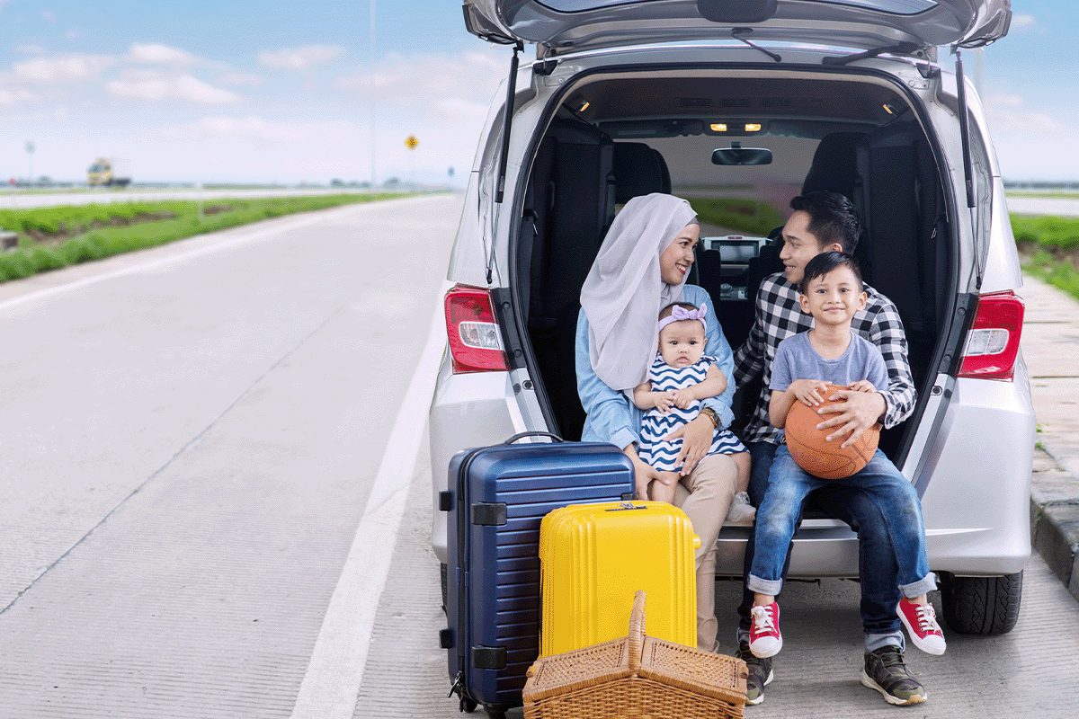 family of four laughing together sitting on the trunk of an SUV.